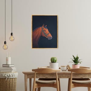 May include: A framed painting of a brown horse's head and neck, set against a dark background. The horse wears a green bridle with gold accents. The frame is gold. The artwork is displayed on a white wall.