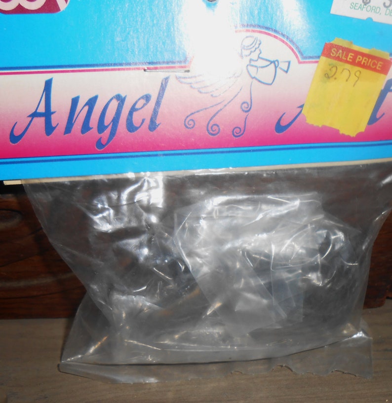 Op de afbeelding: Een plastic zak met een set zwarte metalen engelversieringen. De zak is gelabeld "Angel" en heeft een prijskaartje met de tekst "Sale Price $2.99".