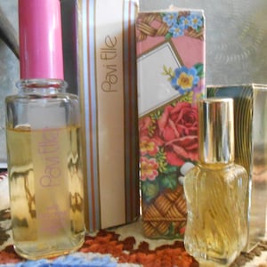 Op de afbeelding: Twee flacons Pavi Elle-parfum met roze en gouden accenten. Eén fles heeft een roze dop en de andere een gouden dop. De dozen zijn versierd met bloemen- en streepmotieven.