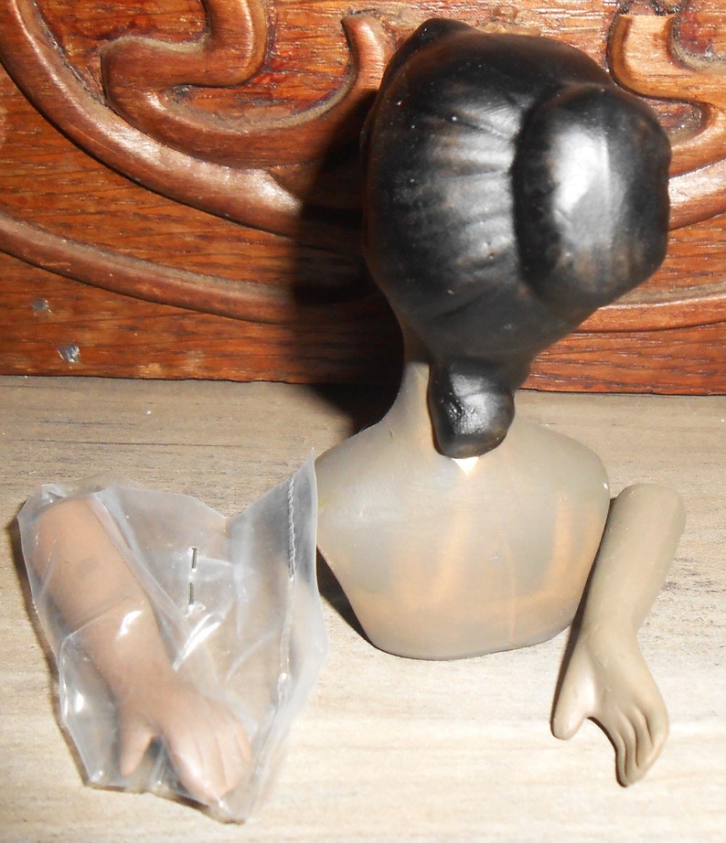 Op de afbeelding: Een porseleinen poppenhoofd met zwart haar in een knot, een naakt torso en twee losse armen. De pop mist haar benen.