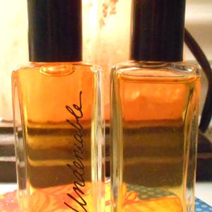 May include: Two clear glass bottles with black caps filled with a light amber liquid. The bottle on the left has the word "Undeniable" written on the label.