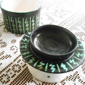 Pode incluir: Um prato de cerâmica preto e verde com um padrão em ziguezague. O prato está empilhado em cima de uma base de cerâmica branca com um furo no centro.