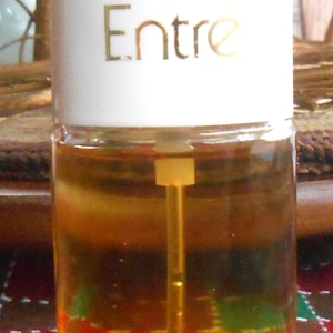 May include: A clear glass bottle with a white cap. The bottle contains a golden-coloured liquid and has the word "Entre" printed on the front. The bottle has a long, thin applicator inside.