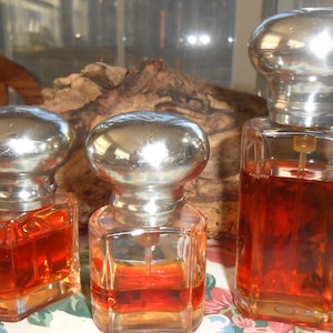 Puede incluir: Tres botellas de vidrio con tapas plateadas y un líquido marrón en su interior. Las botellas son de diferentes tamaños y están sobre una superficie de madera.