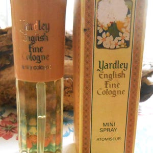 Op de afbeelding: Een klein flesje Yardley English Fine Cologne in een mini-spuitflacon. De fles is van helder glas met een gouden dop en een bloemenmotief. De doos is geel met een bloemenmotief en de tekst "Yardley English Fine Cologne" en "Mini Spray Atomiseur".