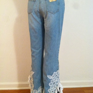May include: Light blue denim jeans with white lace trim at the bottom of the legs. The jeans have a gold label on the back pocket that reads "Miss Sixty Denim".