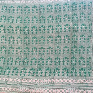 Puede incluir: Una tela blanca con un patrón geométrico verde. El patrón es una forma de diamante repetida con un pequeño punto verde en el centro de cada diamante.