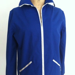 May include: A royal blue zip-up jacket with white piping and zipper. The jacket has two zippered pockets on the front and a white collar.
