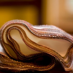 May include: A close-up of a folded brown and white fabric with a decorative trim. The fabric is folded in a wave-like pattern, creating a soft and textured look.