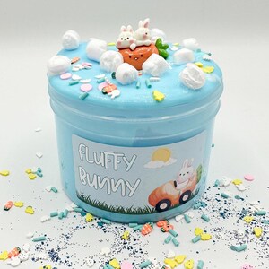 Peut inclure: Un pot de slime bleu avec des guimauves blanches et des vermicelles. Le pot est étiqueté "Fluffy Bunny" avec un lapin de dessin animé dans une voiture.