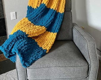 May include: A striped knit throw blanket in mustard yellow and teal blue. The blanket is draped over a gray armchair.