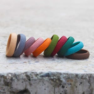 May include: A collection of colorful silicone rings in various shades, including tan, blue, purple, pink, orange, green, red, teal, and brown. The rings have a textured, wood-like appearance.