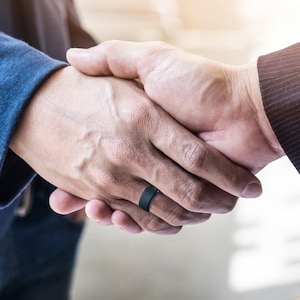 May include: Two people shaking hands, one person is wearing a black silicone ring on their left ring finger.