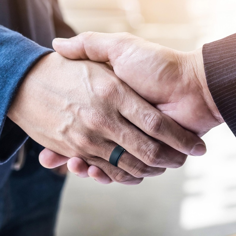 May include: Two people shaking hands, one person is wearing a black silicone ring on their left ring finger.