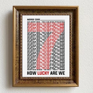 Op de afbeelding: Een ingelijst afdruk met een rood en zwart ontwerp dat "HOW LUCKY ARE WE" in morsecode spelt. De titel "MORSE CODE" staat bovenaan de afdruk.