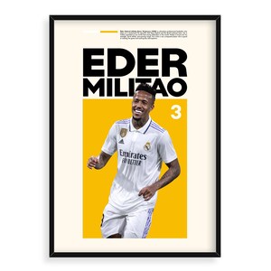 May include: A poster featuring a soccer player in a white jersey with the text "Eder Militao 3" and the words "Emirates Fly Better" on the jersey. The player is standing on a yellow background.