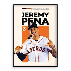 May include: Framed poster of baseball player Jeremy Pena in an Astros uniform, holding a bat. The poster has a cream background with orange and blue accents. The player is smiling, and the word "ASTROS" is visible on the jersey.