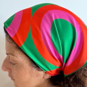 Può includere: Un foulard colorato con un design retrò. Il foulard presenta un motivo di cerchi concentrici in rosso, verde e rosa. Il foulard misura 60 x 60 cm.