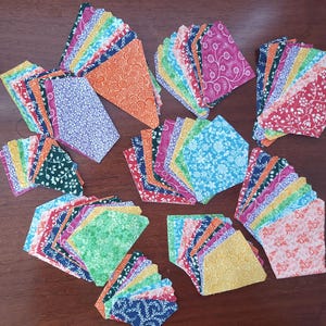 May include: A collection of fabric squares in various colors and patterns, including floral, geometric, and abstract designs. The fabric pieces are arranged in fan-like shapes, showcasing a variety of hues such as blue, green, orange, and pink. Ideal for quilting or crafting projects.