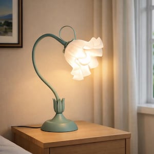May include: A teal-colored bedside lamp with a flower-shaped shade. The lamp has a curved stem and a round base. The flower shade is white and has a ruffled design. The lamp is on a wooden nightstand.