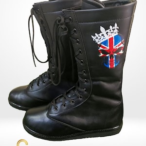 Könnte beinhalten: Paar schwarze Leder-Wrestling-Stiefel. Die Stiefel haben ein Schnürdesign und eine Totenkopf-Grafik mit Krone und der Union-Jack-Flagge an der Seite. Die Stiefel sind hoch und haben eine robuste Sohle.