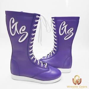 May include: A pair of purple wrestling boots with white laces and soles. The boots have a tall shaft and feature the letters "GS" in a white, stylized font on the side. The boots are designed for athletic performance.