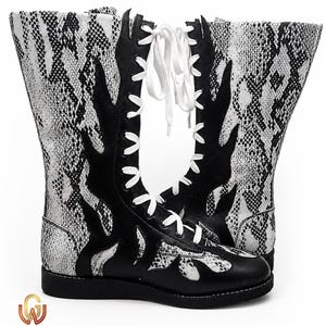 May include: Black and white snake-skin patterned boots with a flame design. The boots have white laces and a black sole. The boots are tall, reaching up the calf. The boots have the text "Wrestle Gears" at the bottom.