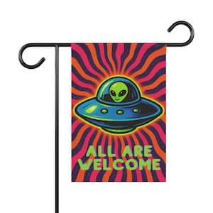 May include: A rectangular garden flag featuring a green alien inside a blue and black flying saucer. The background consists of vibrant red and purple wavy sunburst lines. The text ALL ARE WELCOME is printed in lime green at the bottom.