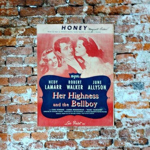 May include: A vintage movie poster for the film "Her Highness and the Bellboy" starring Hedy Lamarr, Robert Walker, and June Allyson. The poster is red, white, and blue with a black and white photo of the actors.