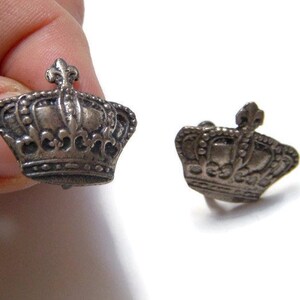 K&ouml;nnte beinhalten: Ein Paar silberne Manschettenkn&ouml;pfe in Kronenform. Die Kronen sind mit komplizierten Designs verziert und haben eine leicht gealterte Oberfl&auml;che.