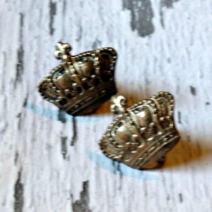 K&ouml;nnte beinhalten: Ein Paar goldfarbene Ohrringe in Kronenform. Die Kronen haben komplizierte Details und ein Fleur-de-lis-Design.