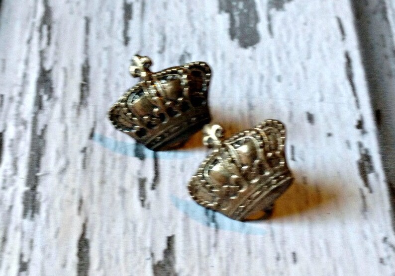 K&ouml;nnte beinhalten: Ein Paar goldfarbene Ohrringe in Kronenform. Die Kronen haben komplizierte Details und ein Fleur-de-lis-Design.