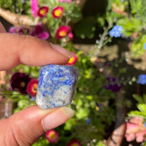 May include: A small, tumbled stone featuring a mottled pattern of deep blue, white, and grey mineral inclusions. The polished surface of the stone displays a smooth, rounded rectangular shape with irregular colour distribution across its entire exterior.
