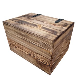 May include: A rustic wooden storage box with a hinged lid and black metal hardware. The box is constructed from light brown wood planks with a visible grain pattern and darker, burnt-looking edges. The box is rectangular and appears to be handmade.