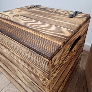 May include: A rustic wooden storage chest with a hinged lid and metal hardware. The chest is constructed from stained wood planks, showcasing the natural grain and knots. The exterior features a dark brown stain, and the chest has a handle on the side.