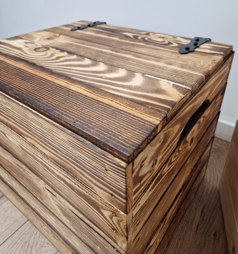 May include: A rustic wooden storage chest with a hinged lid and metal hardware. The chest is constructed from stained wood planks, showcasing the natural grain and knots. The exterior features a dark brown stain, and the chest has a handle on the side.