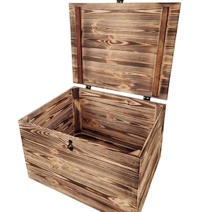 K&ouml;nnte beinhalten: Offene Holzkiste mit Scharnierdeckel. Die Truhe besteht aus gebeiztem Holz mit sichtbarer Maserung und einem dunklen Metallverschluss. Der Deckel ist angehoben und gibt den Innenraum frei. Eine dekorative Aufbewahrungsl&ouml;sung.