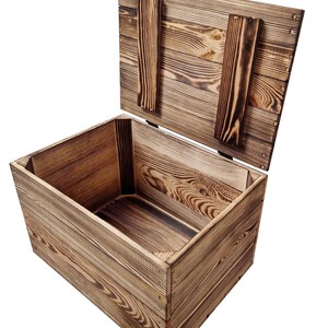 May include: A rustic wooden storage box with a hinged lid, open to reveal the interior. The box is constructed from light brown wood with visible grain and darker, charred accents. The lid is propped open with two wooden supports.