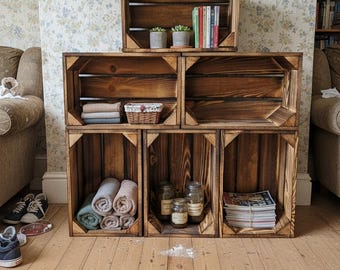 Pode incluir: Um conjunto de seis caixas de madeira escura dispostas como prateleiras. As caixas contêm livros, plantas, toalhas, frascos e revistas. A estante está colocada contra um fundo de papel de parede floral.