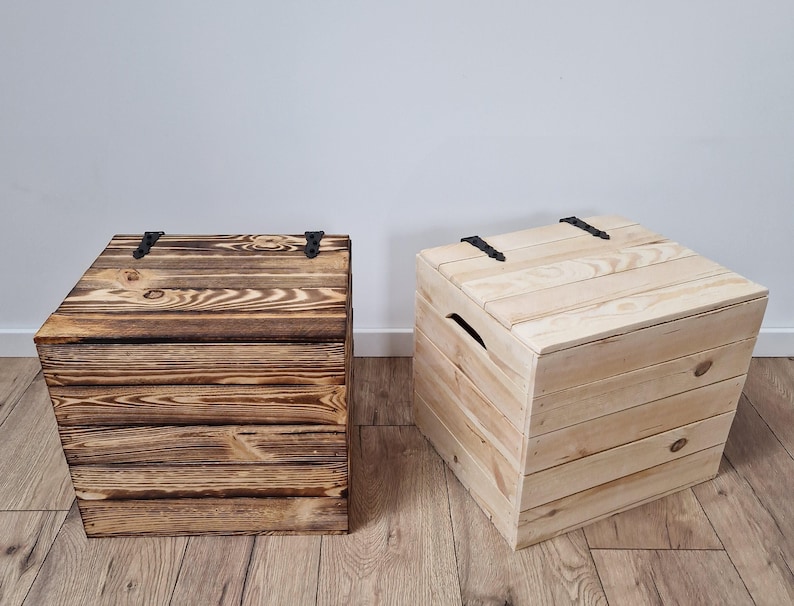 May include: Two wooden storage chests. One is stained a dark brown, the other is natural wood. Both have hinged lids with black metal hardware. The chests are constructed from horizontal wooden planks and are suitable for various storage needs.
