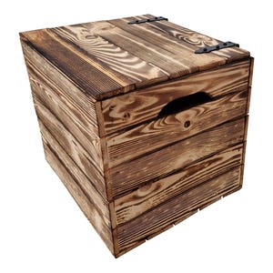May include: A rustic wooden storage box with a hinged lid and a handle cut into the side. The box is constructed from horizontal wooden planks with a dark brown finish, and black metal hinges.