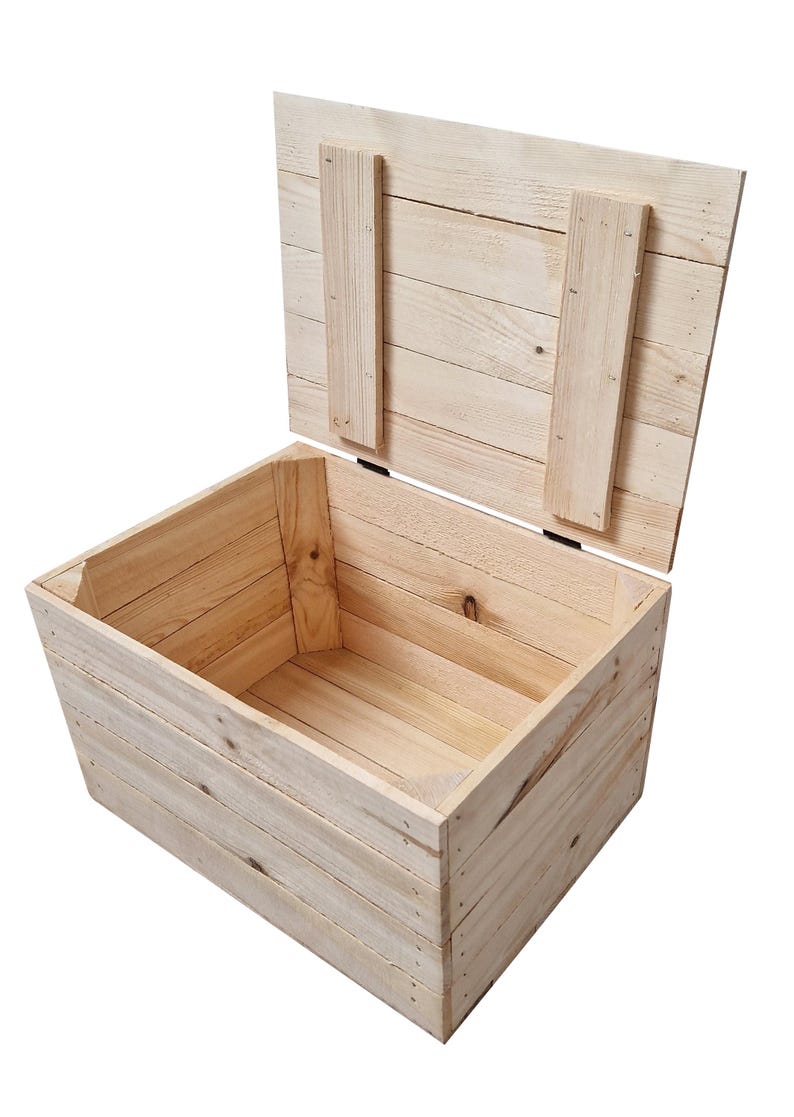 May include: An open, light-colored wooden storage chest with a hinged lid. The chest is constructed from planks of wood, with the lid secured by two vertical wooden supports. The interior of the chest is visible, showcasing the natural wood grain.
