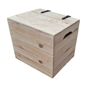 May include: A light-colored wooden storage box with a hinged lid and black metal hinges. The box is constructed from planks of wood, with a handle cut into the side. The wood has visible knots and grain.