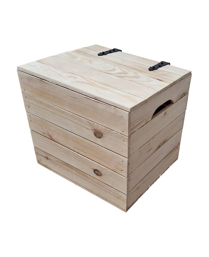 May include: A light-colored wooden storage box with a hinged lid and black metal hinges. The box is constructed from planks of wood, with a handle cut into the side. The wood has visible knots and grain.