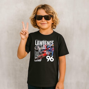 May include: Black t-shirt featuring a motocross image with the name "LAWRENCE" and the number "96". The shirt has a graphic of a rider on a red and blue motorcycle. The person in the image is wearing sunglasses and making a peace sign.