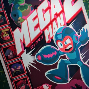 May include: Mega Man 2 poster featuring the character in a blue and red suit, firing a blast. A green dragon and other characters are also shown. The title is in large white letters with a red outline, and Japanese text is included.