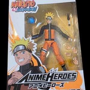 Op de afbeelding: Een Anime Heroes actiefiguur van Uzumaki Naruto uit Naruto Shippuden in de doos. De figuur is oranje en zwart, met verwisselbare handen en accessoires. De verpakking toont karakterkunst en het serielogo.