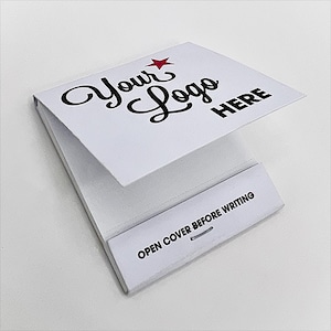 Può includere: Un blocco note bianco con la scritta "Your Logo HERE" in corsivo nero e una stella rossa. La parte inferiore recita "OPEN COVER BEFORE WRITING". Il blocco note è aperto, rivelando le pagine bianche.