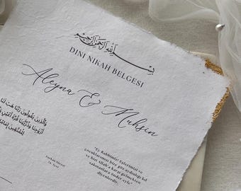 Può includere: Un certificato Dini Nikah Belgesi rettangolare stampato su carta bianca testurizzata con bordi irregolari e accenti in foglia d'oro. Il documento presenta testo nero, inclusi i nomi Aleyna e Muhsin, con linee per firme e dettagli.