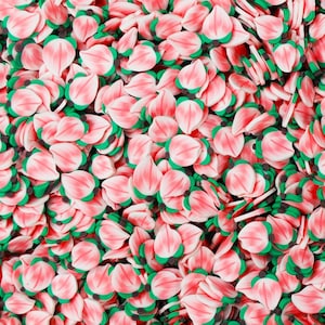 以下が含まれることがあります： 小さな花型のポリマークレイの破片のクローズアップ。 花びらは白のアクセントが入ったソフトピンクで、ベースは小さな黒い点が付いた緑色です。 クラフトに最適です。